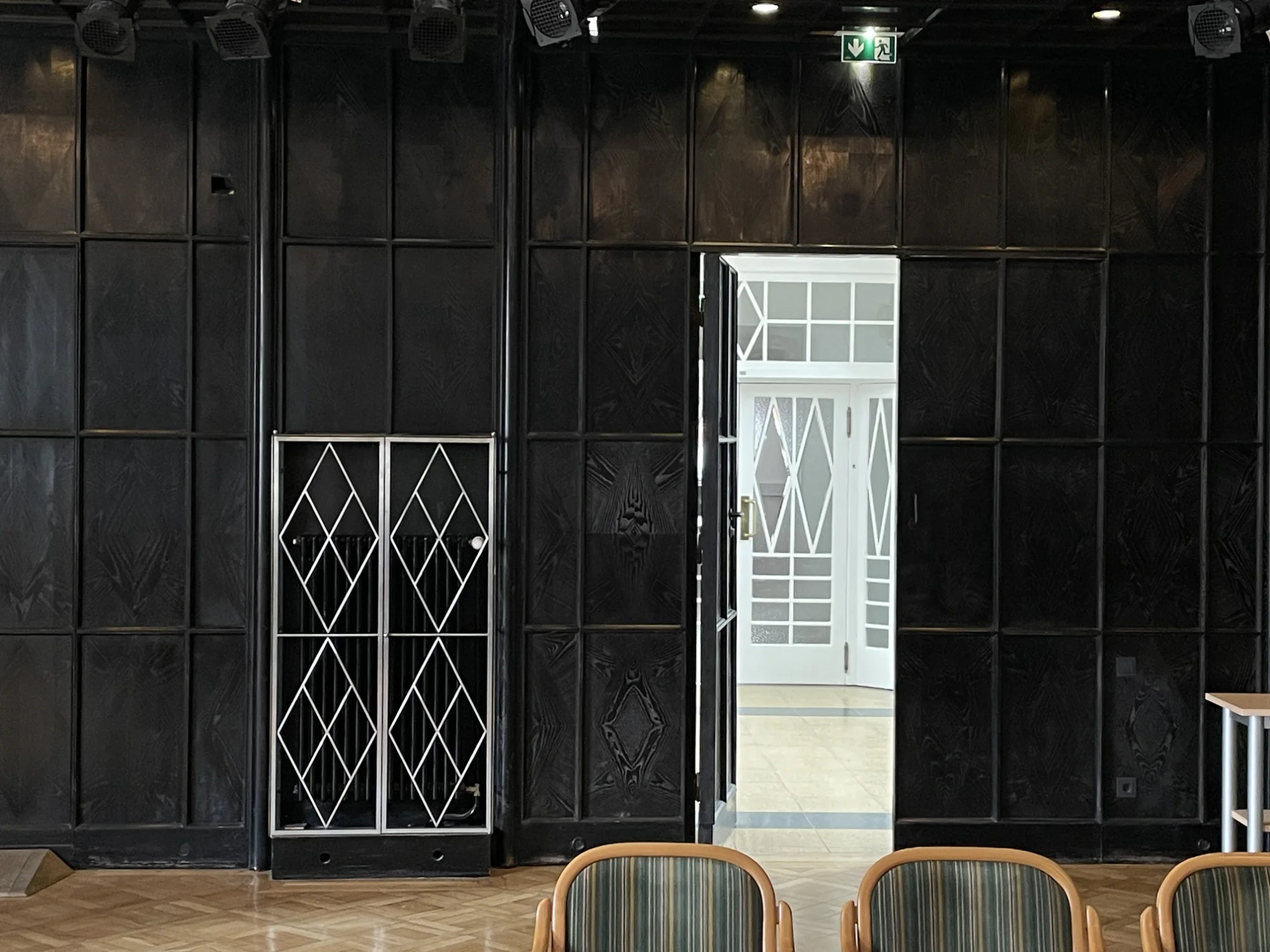 A rich decorated dark wooden wall. The photographer is looking through the door to a light painted sunny room.
