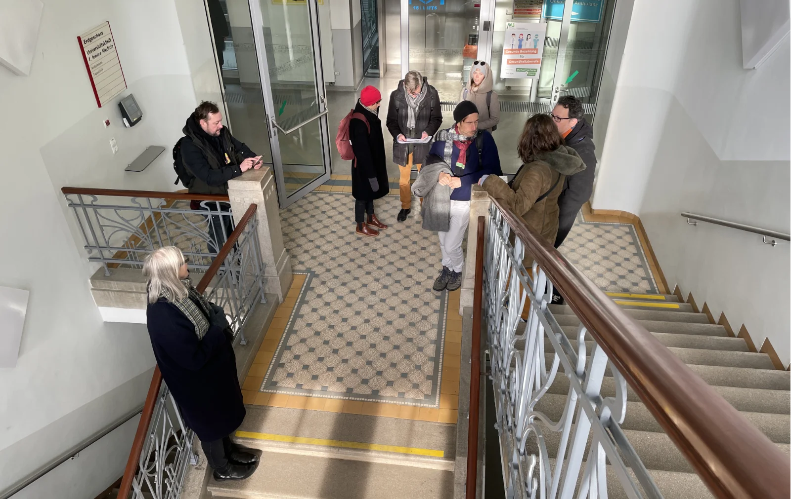 Seven persons are discussing while standing in the staircase of an old hospital. The photo is seen from above.